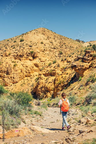 A woman with a backpack walks along a trail in a deserted canyon with red rocks. Hiking path and the dangers of solo trekking