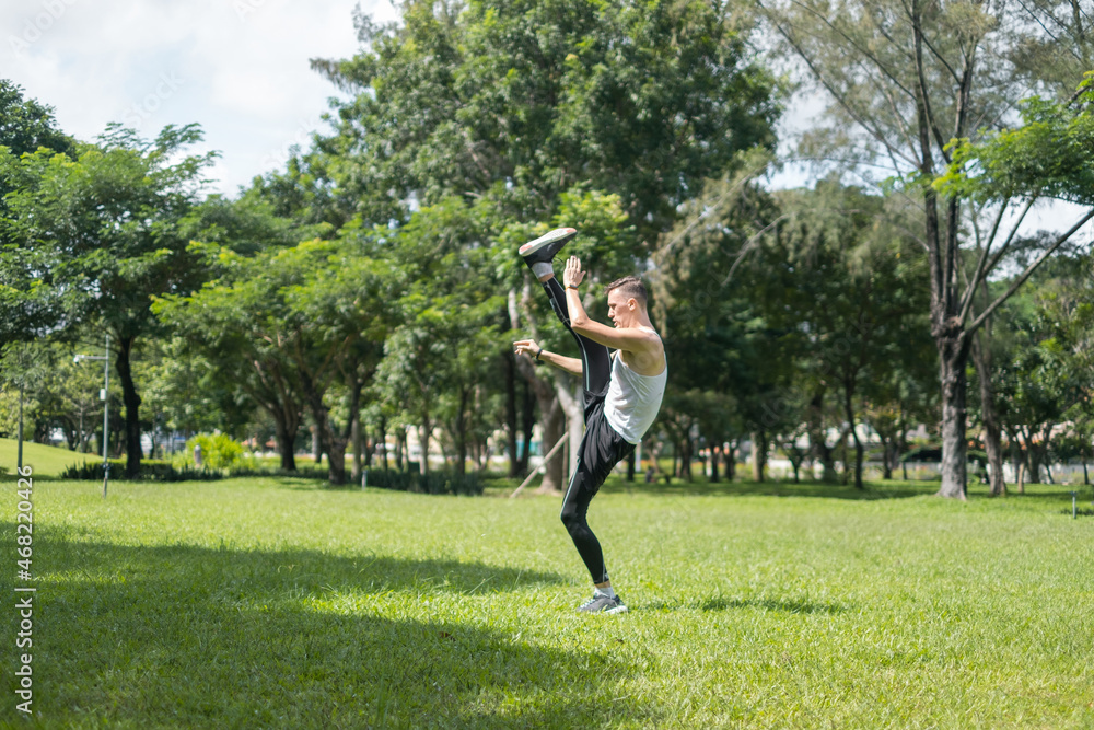 Sporty active young man in sportswear doing sport exercises in the park. One leg raised up. Healthy lifestyle concept, sport outdoor, training