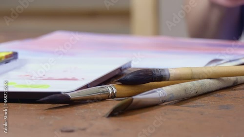 The artist paints with a brush on paper in watercolor.