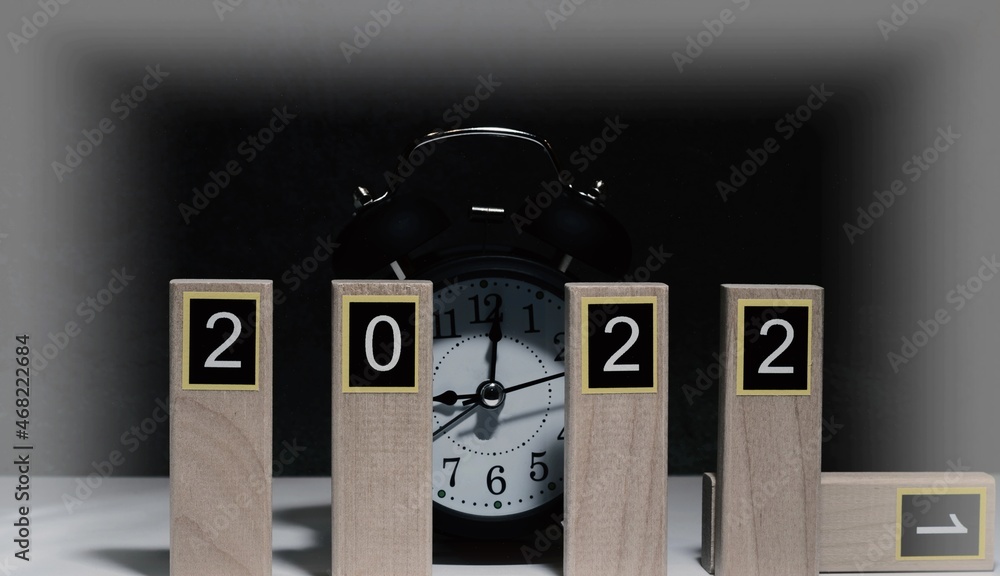 Numbers 2022 on wooden planks and black retro alarm clock on dark background with creative vignetting. New Year holidays concept.