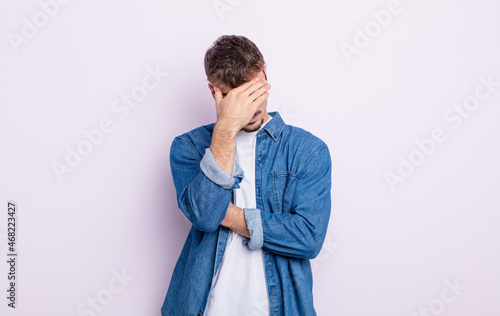 young handsome man looking stressed, ashamed or upset, with a headache, covering face with hand
