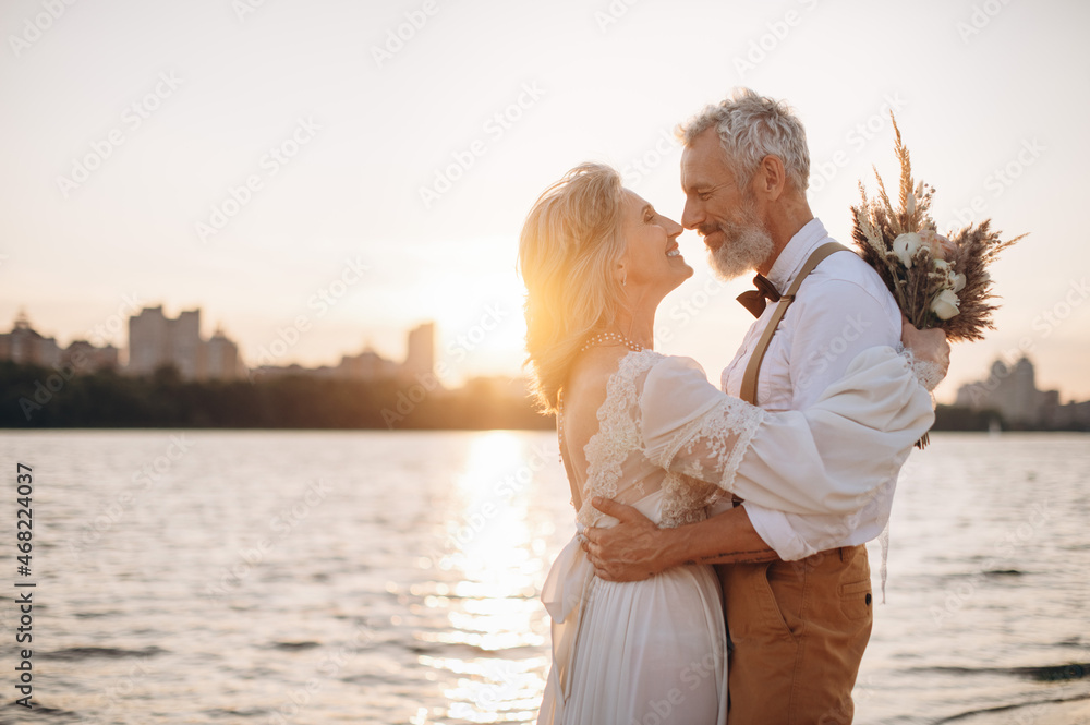 Obraz premium Happy elderly couple in wedding dress looking at each other in sun.