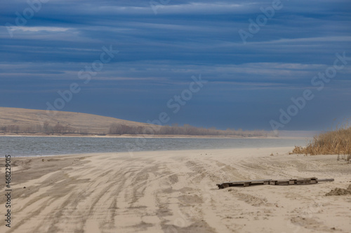 A dramatic view of an empty autumn beach on a cold river in November.