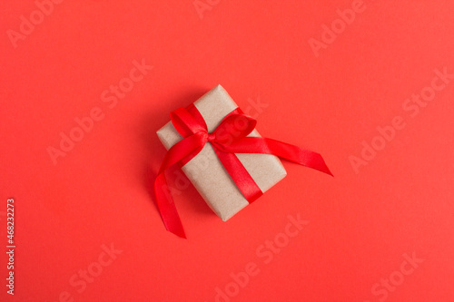 Gift box with tied red bow on the red background. Top view. Copy space.