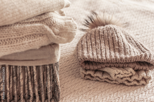 Stack of cozy knitted wool clothes in wicker basket, sweater, jumpers, hat . Hygge mood, cold weather concept. Autumn or winter background.