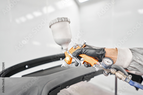 Paint Gun is designed by professionals for a professional quality paint job. Worker painting parts of the car in special painting chamber, wearing costume and protective gear. Car service station.
