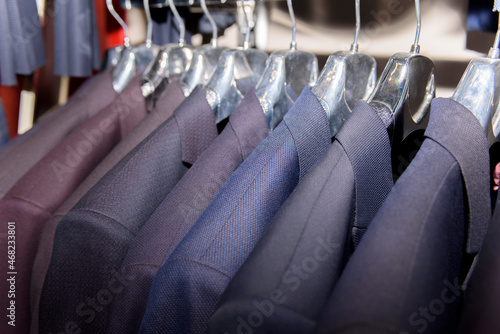 Men's suits on hangers in a men's store. A row of hanging men's suits and jackets in the closet.