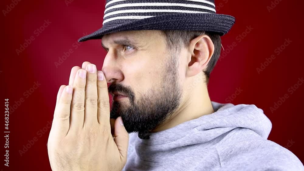 bearded man in a black hat stands sideways raises his head and pleadingly puts bearded man in a black hat stands sideways raises his head and pleadingly puts
