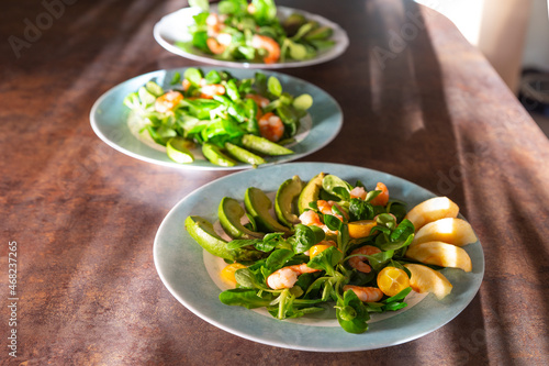 Served fresh green salad with shrimps, avocado, apples and kumquat in the plates on a table