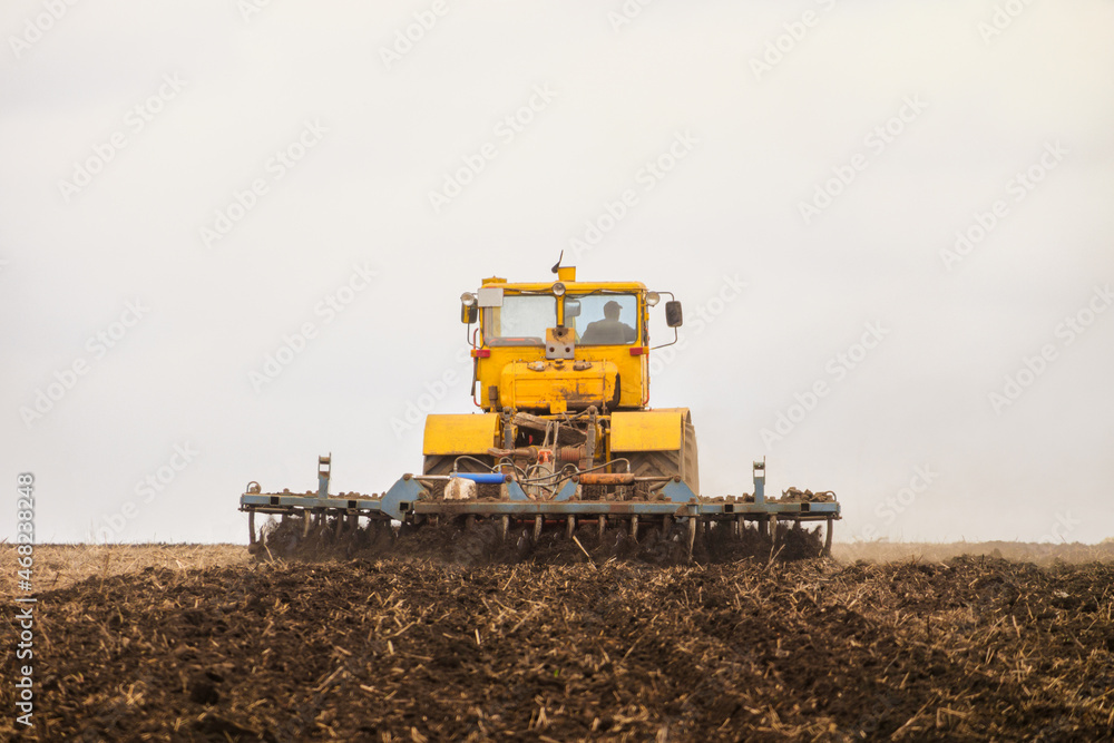 Fototapeta premium Tractor pulls disc harrow. Soil cultivation. Back view.