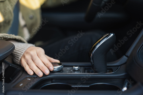 Young caucasian woman hand's turns the control wheel of a modern multimedia system in the car. Vehicle interior. Adding volume. Freedom of movement concept. Selective focus.