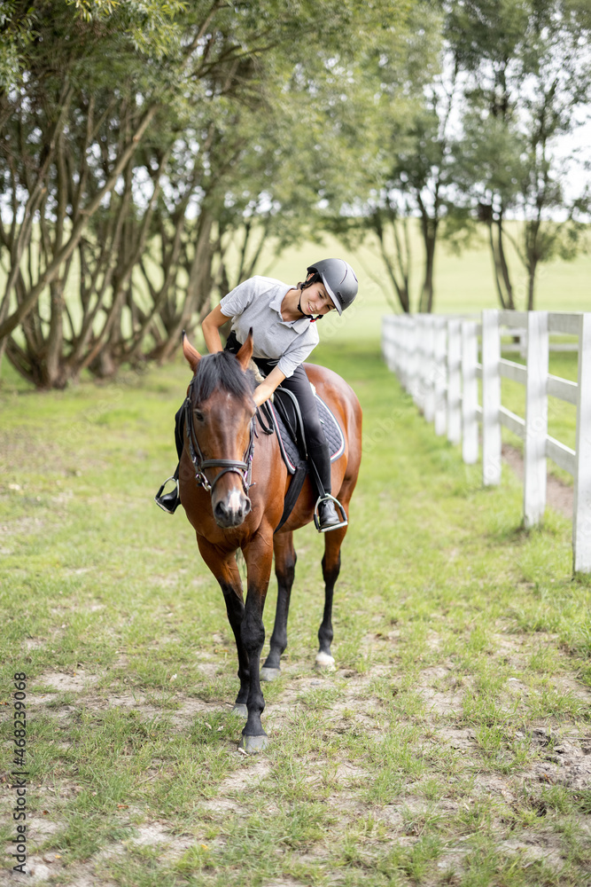 Female horseman riding brown Thoroughbred horse in green meadow in countryside. Concept of rural resting and leisure. Idea of green tourism. Young european woman. Beautiful landscape on sunny day Female horseman riding brown Thoroughbred horse in green meadow in countryside. Concept of rural resting and leisure. Idea of green tourism. Young european woman. Beautiful landscape on sunny day