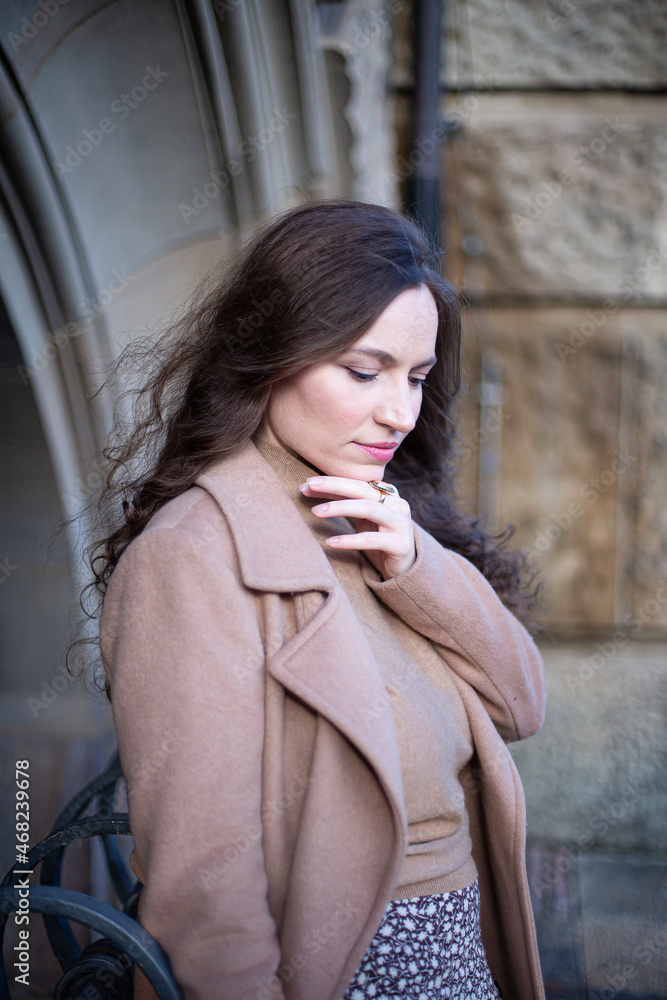 Thinking pretty woman with curly hair near stone wall in autumn park