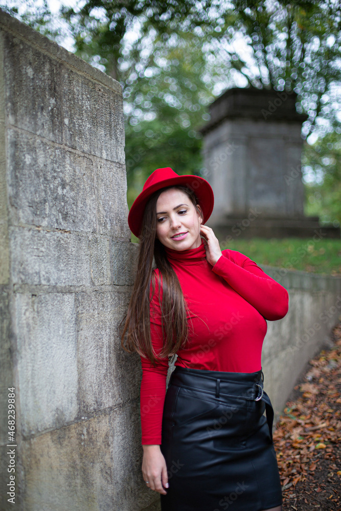 White woman with long dark hair in bright red near stone wall in autumn park