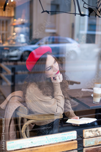 Pretty woman with curly hair in red french beret outside the cafe window