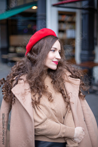 Portrait of smiling pretty woman with curly hair in red french beret walking in the street