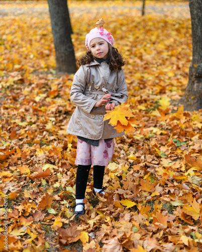 Portrait of a unhappy child in an autumn park. Sad girl standing with fallen yellow leaves. © soleg