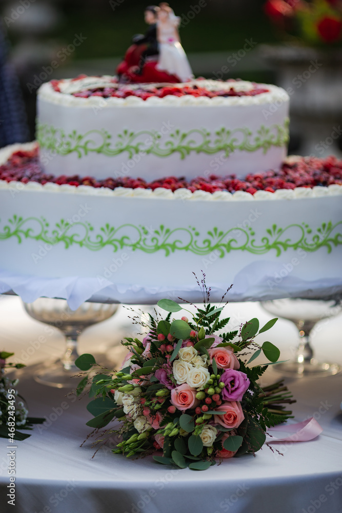 Traditional white wedding raspberry cake with bouquet on white table. Wedding delicious fruit cake dessert Traditional white wedding raspberry cake with bouquet on white table. Wedding delicious fruit cake dessert