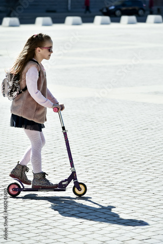 A cute girl with a backpack on a scooter rides around the city.