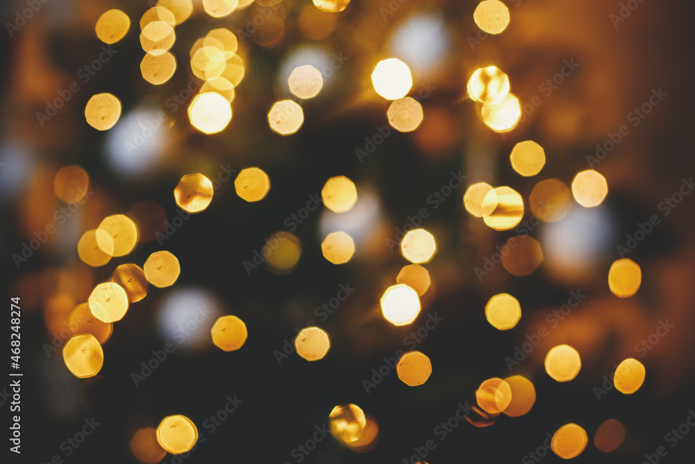 Golden Christmas lights bokeh. Christmas abstract background, glowing illumination on decorated christmas tree defocused in evening festive room. Merry Christmas and Happy holidays