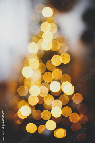 Golden Christmas tree lights defocused in evening festive room. Christmas background, glowing illumination bokeh. Atmospheric christmas eve. Merry Christmas and Happy holidays