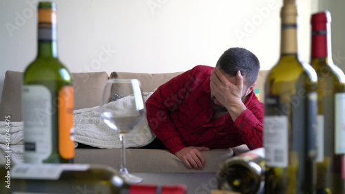 Man wakes up hungover in front of empty wine bottles. Man with drinking issues in the morning after the party photo