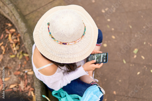 young female tourist in a park sending a text message from her cell phone, wearing a hat, overhead shot, unrecognizable model
