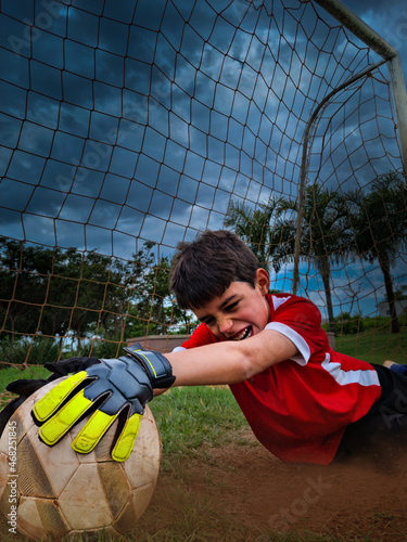 Boy struggles to catch the ball playing football (soccer) as a goalkeeper with dramatic sky in the background