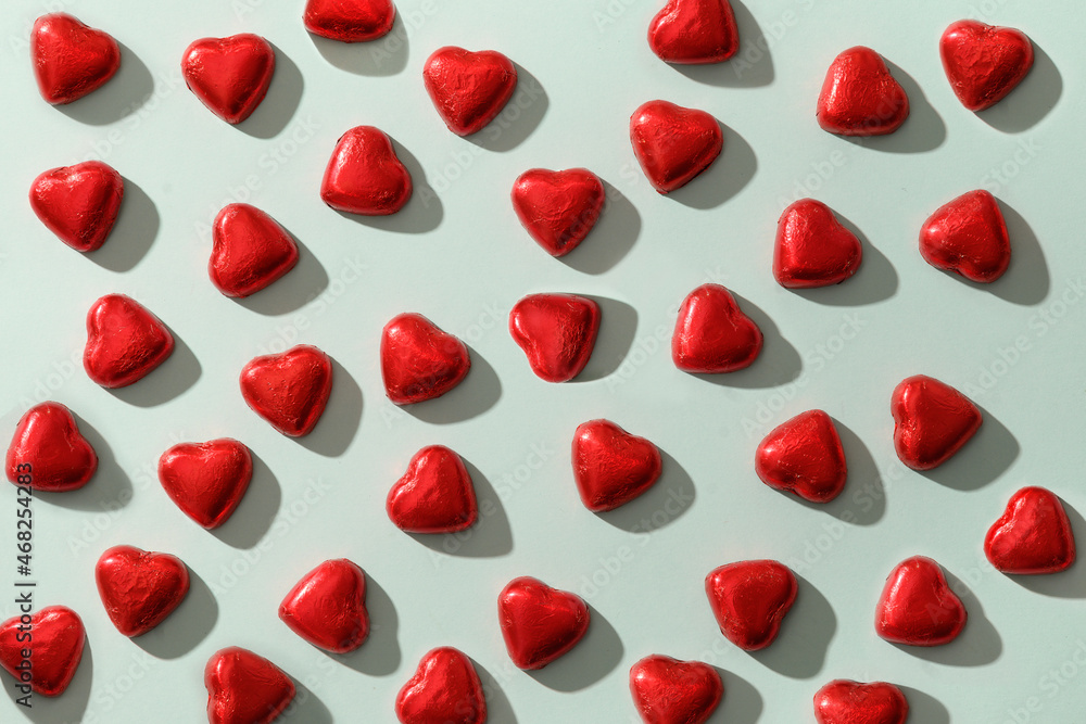 Pattern of romantic chocolate sweets as heart in red foil on blue background. Valentine's day greeting card. Love concept. Pattern of romantic chocolate sweets as heart in red foil on blue background. Valentine's day greeting card. Love concept.
