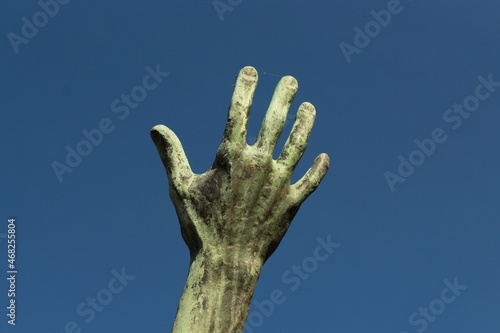 geöffnete Hand greift nach oben in den blauen Himmel (Skulptur)