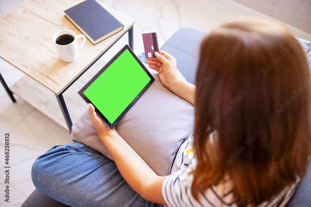 Obraz premium Woman shopping on tablet computer using credit card sitting in sofa. Online shopping