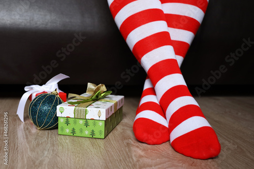 Female legs in Christmas socks on a floor near the gift boxes. Woman sitting on a bed in home, New Year celebration