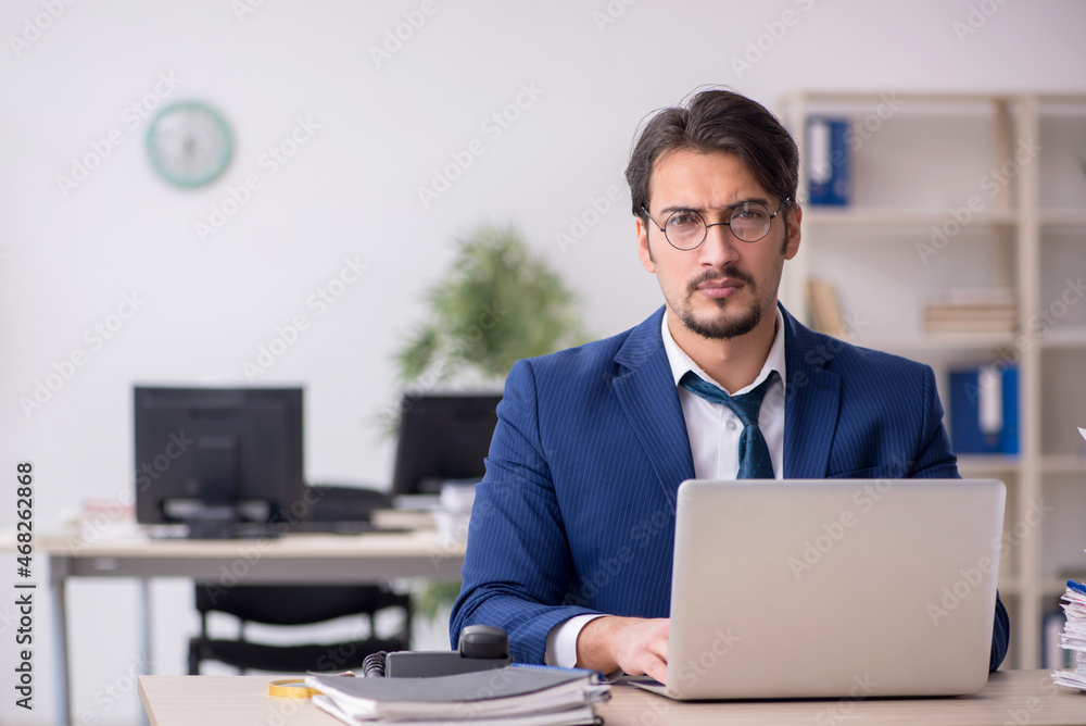 Young male employee unhappy with excessive work in the office Young male employee unhappy with excessive work in the office