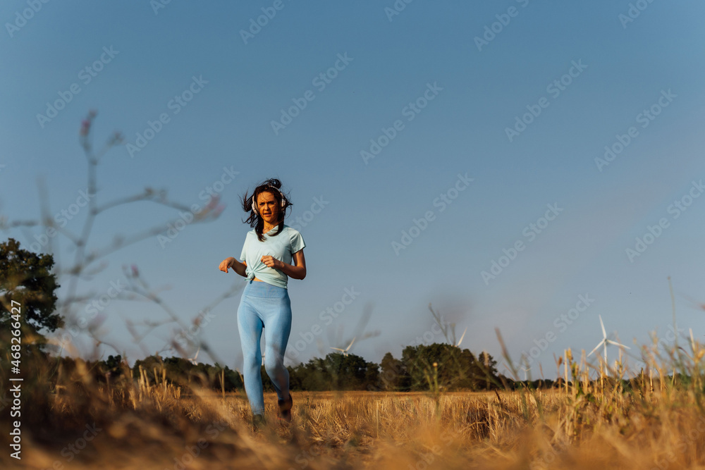 middle-aged beautiful young woman running with windmills in the background in a lot of wind and music headphones middle-aged beautiful young woman running with windmills in the background in a lot of wind and music headphones