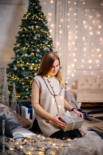 A young woman in a sweater with long beautiful hair sits and laughs in front of Christmas gifts. Happy New Year
