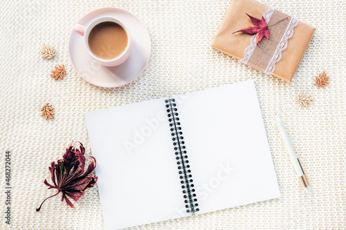 Blank open notepad, coffee cup, gift in a box, pen and autumn leaves on white knitted plaid background. Top view, flat lay