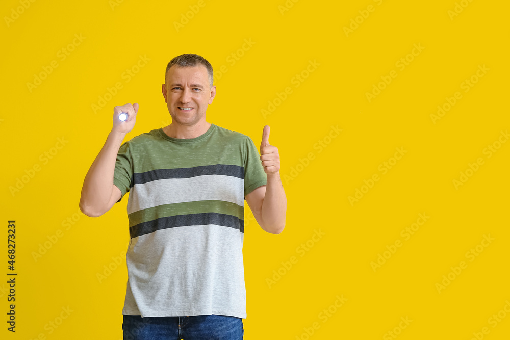 Mature man with LED torch showing thumb-up on yellow background Mature man with LED torch showing thumb-up on yellow background