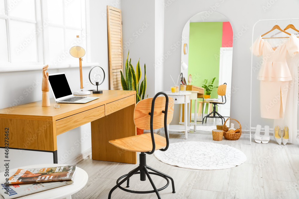 Fototapeta premium Interior of light room with modern workplace, big mirror and female clothes