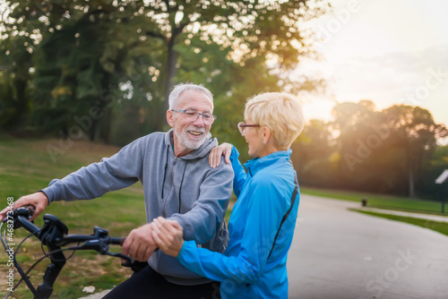 Cheerful active senior couple with bicycles walking through park together. Perfect activities for elderly people.