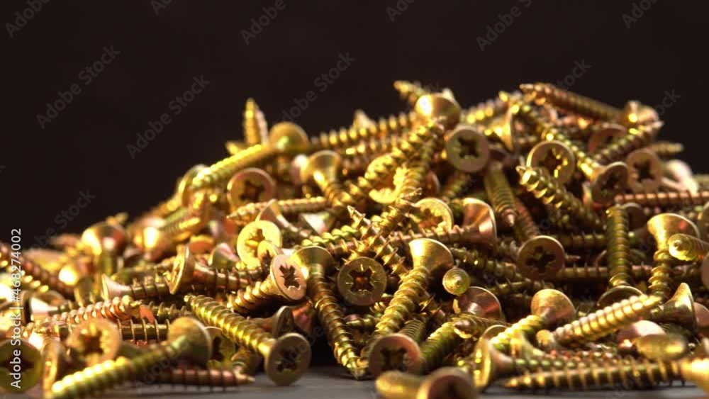 Golden screws rotate on a black background and cross head screws, construction supplies self-tapping screws or bolts Golden screws rotate on a black background and cross head screws, construction supplies self-tapping screws or bolts