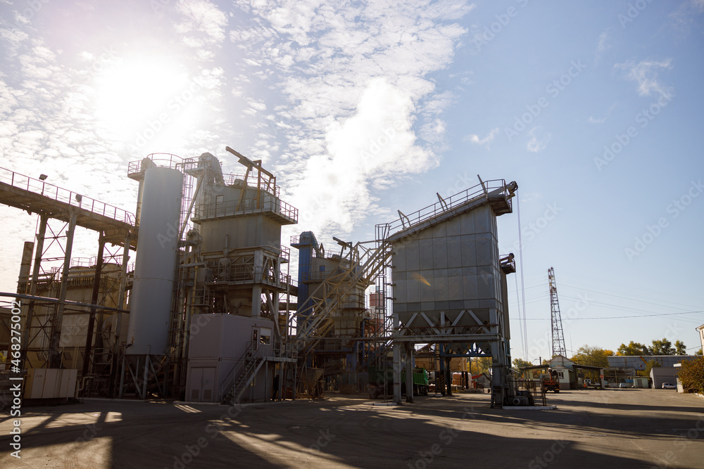 Obraz premium Manufacturing plant with industrial buildings, equipment and ladders under sky with clouds and sun