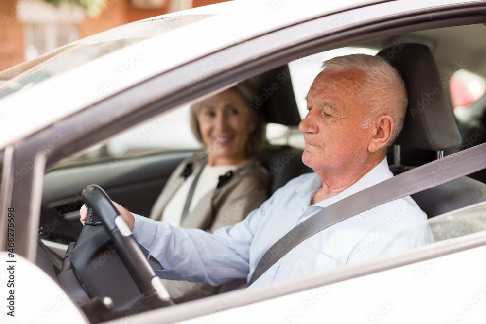 Elderly man and woman driving a car in the city. Man driving a car