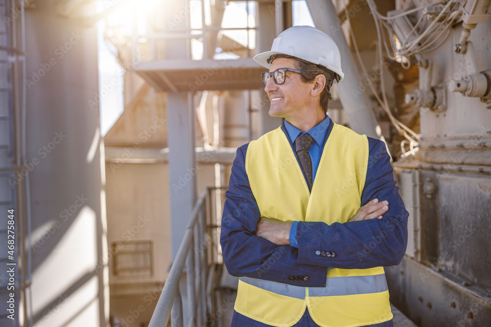 Joyful matured man wearing safety helmet and work vest while keeping arms crossed and smiling Joyful matured man wearing safety helmet and work vest while keeping arms crossed and smiling