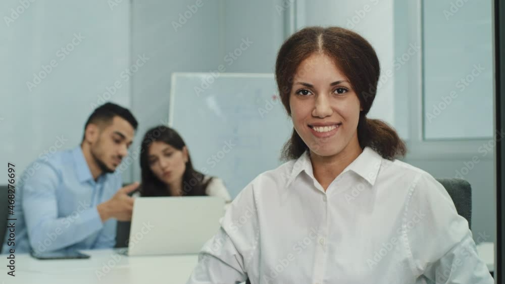 Portrait smiling businesswoman sitting in modern business office with multicultural professionals team, looking at camera, waving hello. Friendly hr manager or leader greeting or welcoming new worker Portrait smiling businesswoman sitting in modern business office with multicultural professionals team, looking at camera, waving hello. Friendly hr manager or leader greeting or welcoming new worker