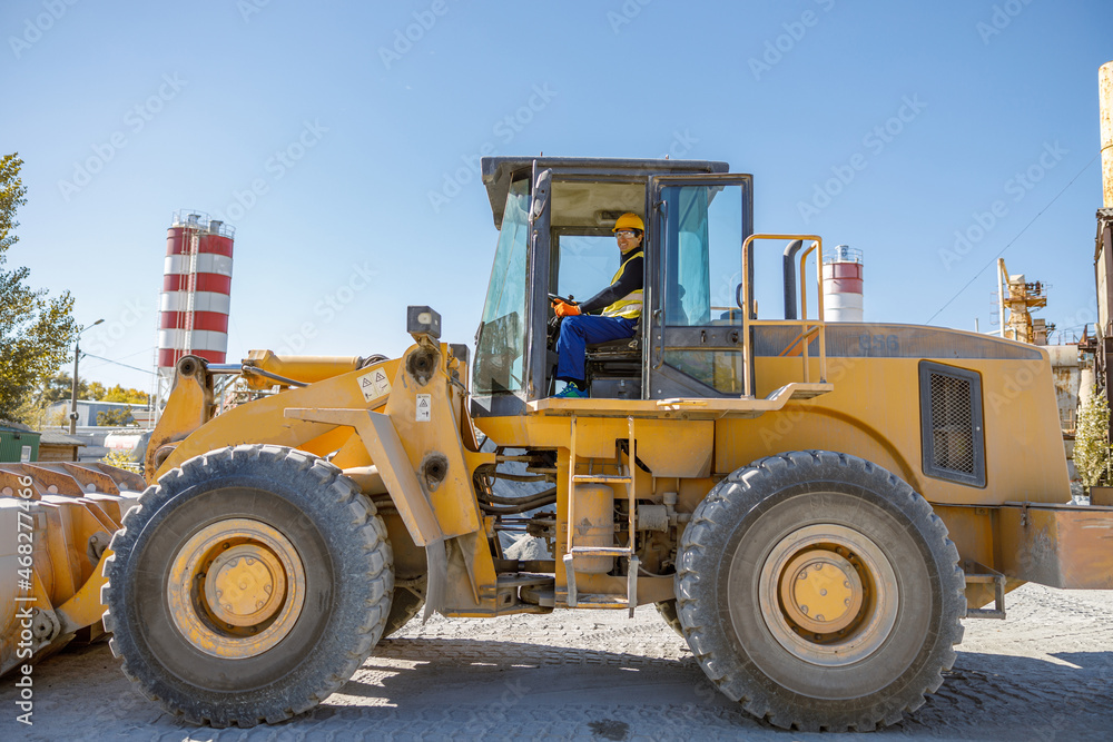 Joyful male worker looking at camera and smiling while sitting in tractor driver cabin at industrial plant