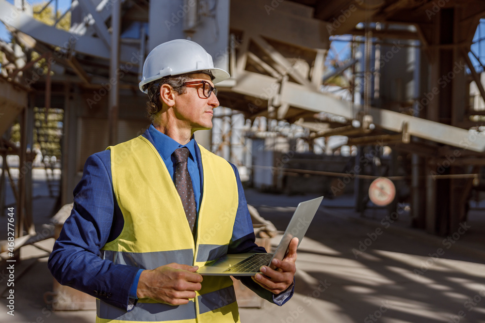 Matured man engineer wearing safety helmet and work vest while holding modern notebook Matured man engineer wearing safety helmet and work vest while holding modern notebook