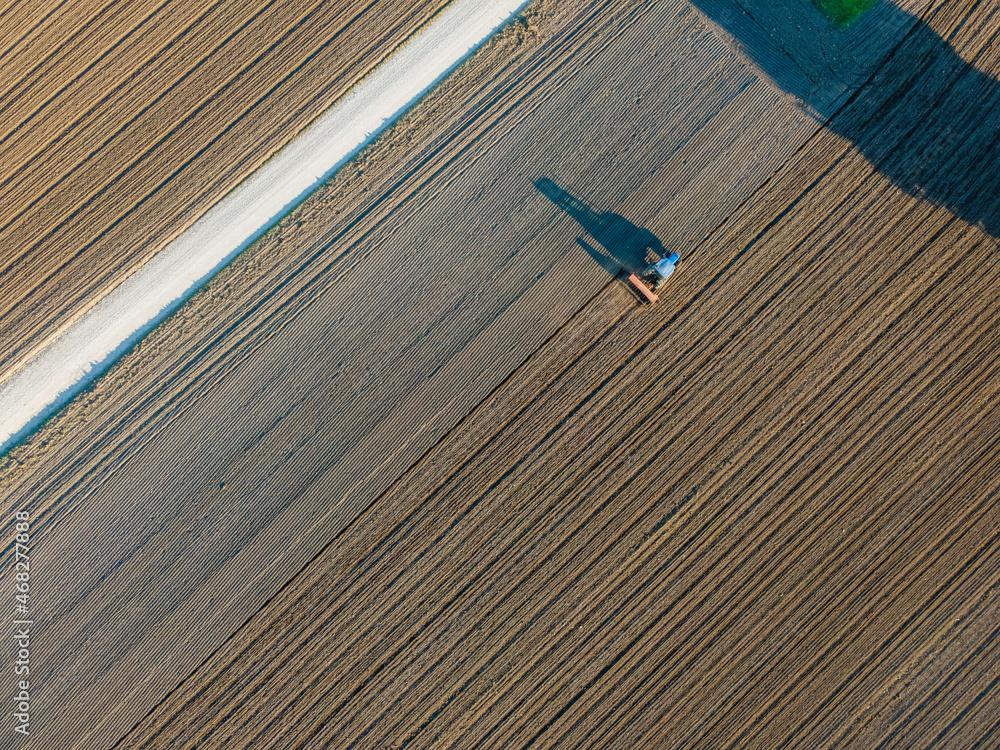 Aerial view of a tractor working in an agricultural field at sunset near Aquileia, Udine, Friuli Venezia Giulia, Italy.