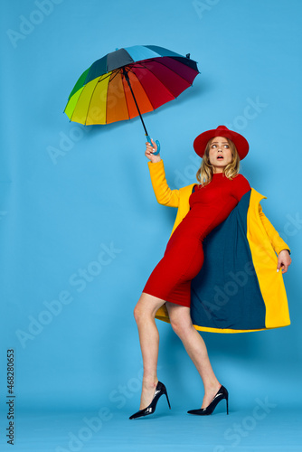 woman in yellow coat multicolored umbrella posing blue background