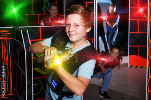 Emotional teen boy with laser pistol playing laser tag with his family on dark room © JackF