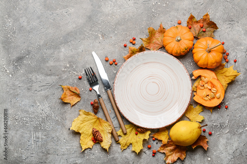 Composition with table setting, pumpkins and autumn leaves on grey background